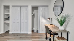 A room with a wooden desk, a chair, a potted plant, a mirror, and white double doors leading to a closet.