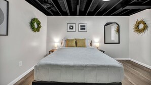 A modern bedroom with a large bed, two bedside tables, wall-mounted artwork, and a ceiling light.