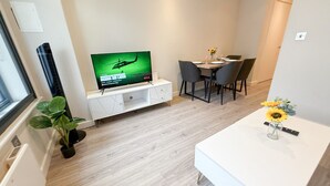 A modern living room with a flat-screen TV, a dining area with a table and chairs, and a small potted plant. - Charming 1 bedroom flat with FAST Wi-Fi near The Shard and Elephant & Castle (London)