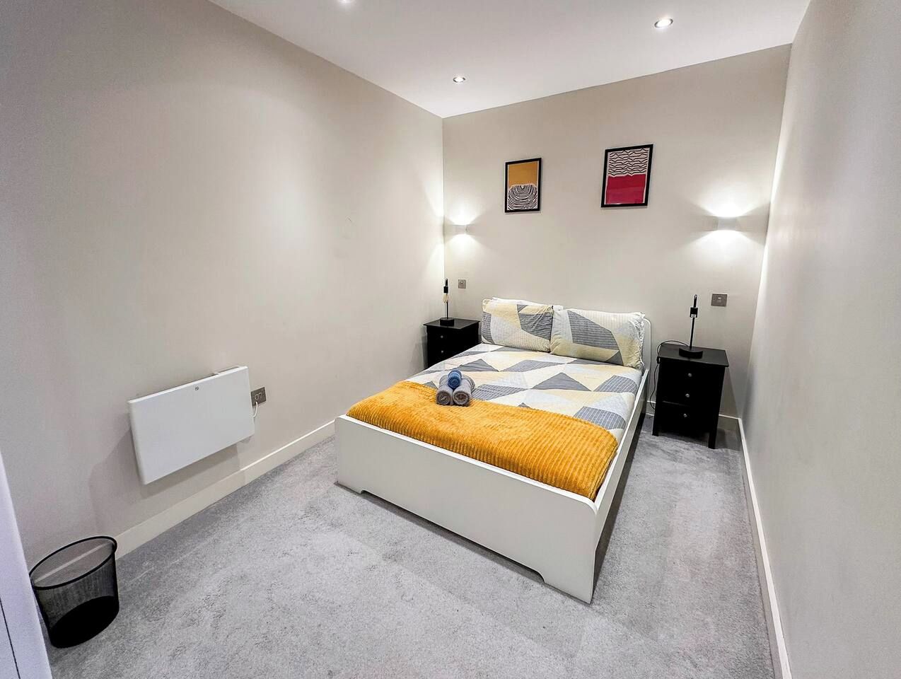 A bedroom with a bed, bedside tables, a radiator, and wall-mounted light fixtures.