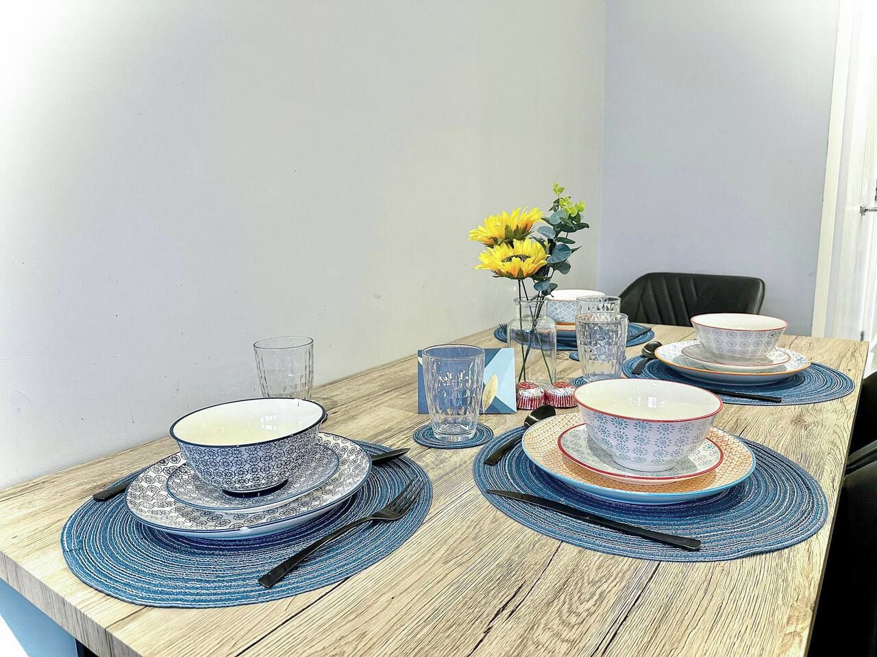 A dining table set with blue and white patterned plates, clear glasses, and a vase with yellow flowers.