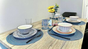 Una mesa de comedor dispuesta con platos de diseño azul y blanco, copas de cristal y un jarrón con flores amarillas.