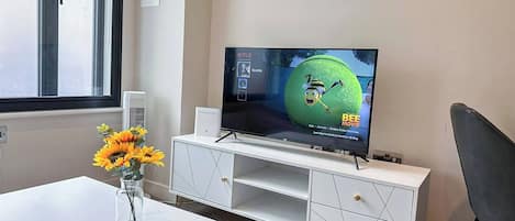 A modern living room with a flat-screen TV on a white entertainment unit, a vase of sunflowers on a white table, and a remote control.