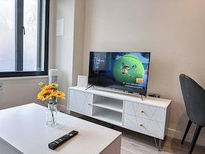 A modern living room with a flat-screen TV on a white entertainment unit, a vase of sunflowers on a white table, and a remote control.