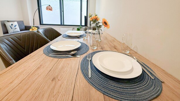 A dining table set with plates, cutlery, and glasses, with a view of a window and a sofa in the background. - Charming 1 bedroom flat with FAST Wi-Fi near The Shard and Elephant & Castle (London)