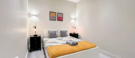 Un dormitorio moderno con una cama blanca, dos mesitas de noche y un cabecero.