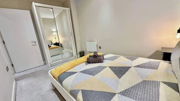 A bedroom with a bed, a wardrobe, a mirror, and a bedside table.
