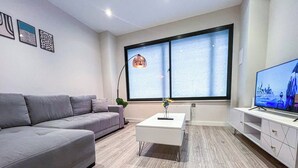 Una sala de estar moderna con un sofá gris, una mesa de centro blanca y un televisor sobre un mueble.