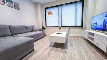 A modern living room with a grey sofa, a white coffee table, and a TV on a stand.