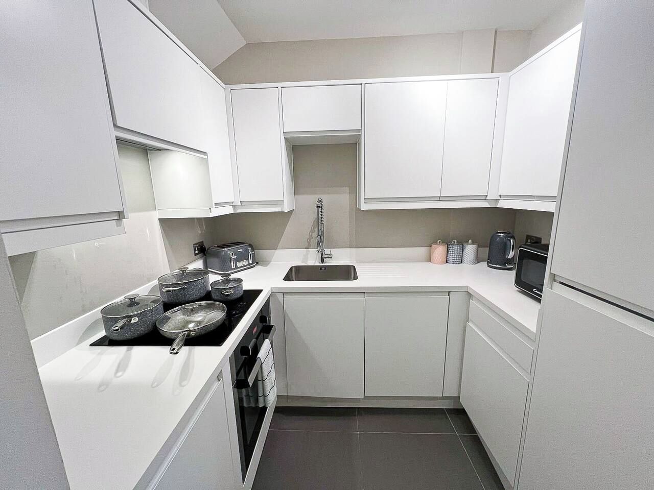 A compact kitchen with white cabinets, a sink, a stove, and a microwave.