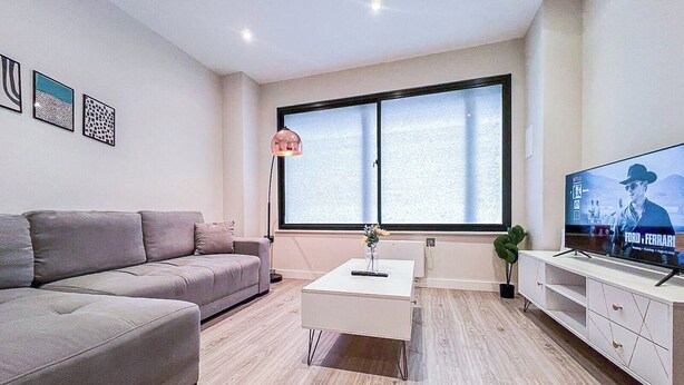 Una sala de estar moderna con sofá, mesa de centro, televisor y una obra de arte en la pared.