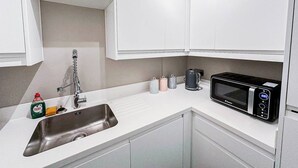 Una cocina moderna con armarios blancos, un lavamanos de acero inoxidable, un microondas y una tetera.