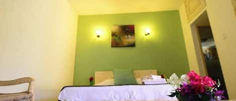 Quarto de hotel com uma cama, uma mesinha com um vaso de flores e duas luminárias na parede.