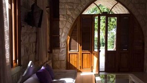 Una habitación acogedora con pared de piedra, puerta de madera que da al exterior y un rincón de estar con cojines.