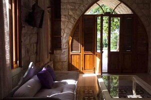 Quarto acolhedor com parede de pedra, porta de madeira que dá para o exterior e um espaço de estar com assentos acolchoados.