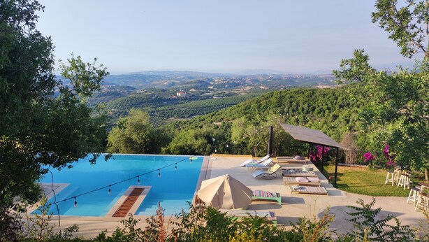 Zona de piscina con sillones de descanso y una pérgola, rodeada de follaje y con vistas a un paisaje pintoresco.