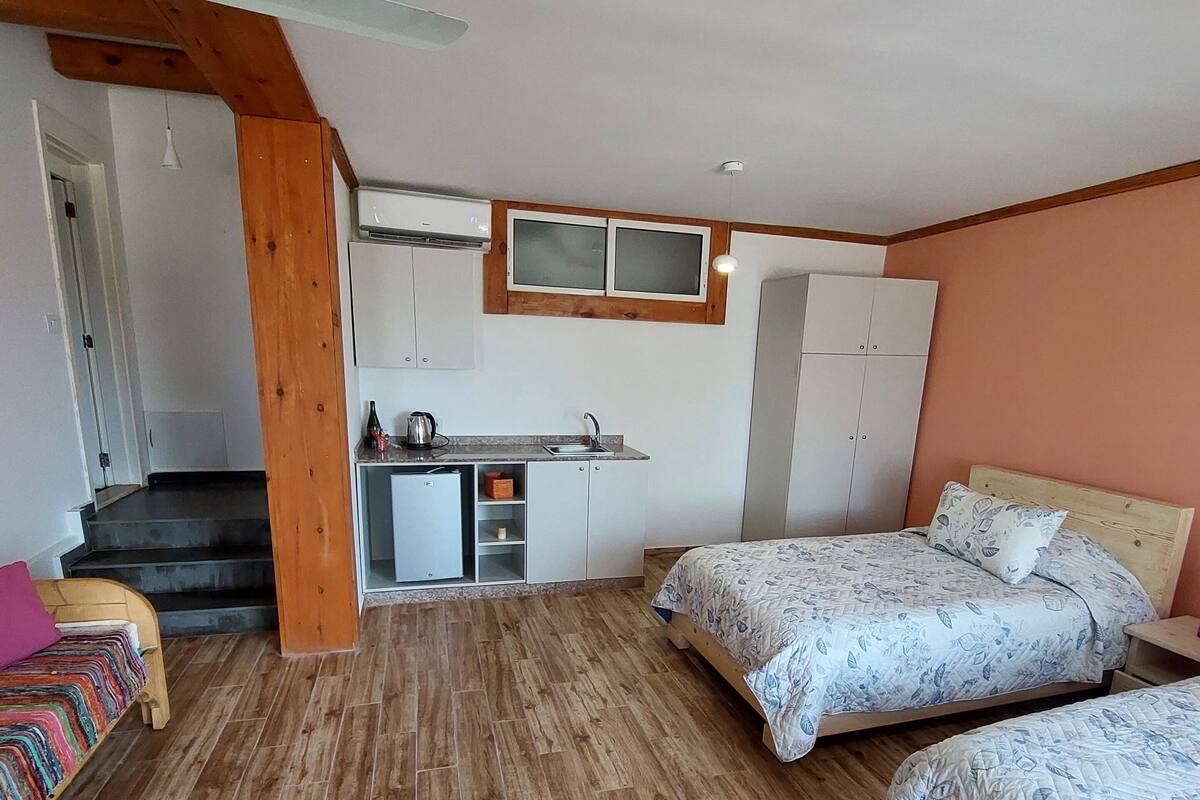 A bedroom with two beds, a small kitchenette, and a wooden staircase.