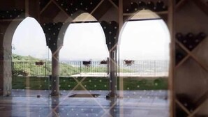Un espacio al aire libre cubierto con tres arcos, piso de baldosas y vista a un paisaje cercado.