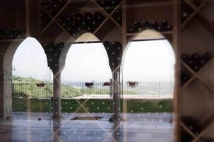 Área externa coberta com três arcos, piso de azulejos e vista para uma paisagem cercada.