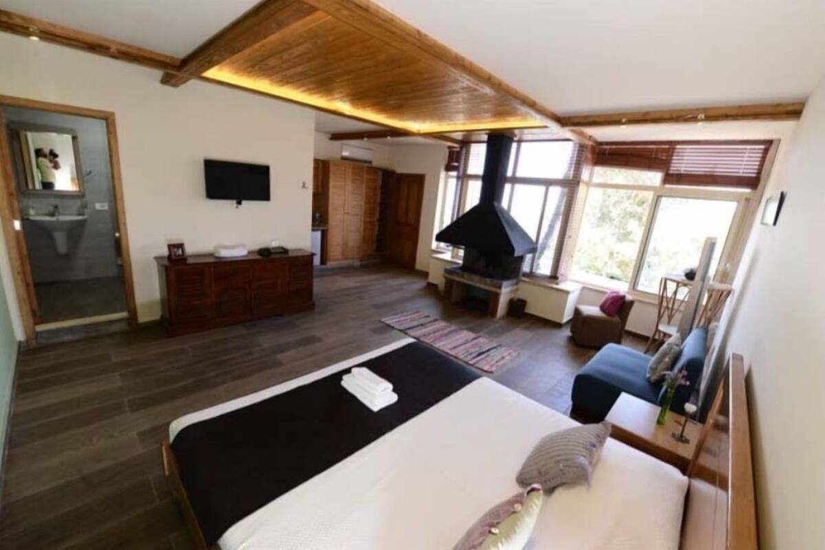 A bedroom with a large bed, a wooden ceiling, a TV, a fireplace, and a view of the outdoors.