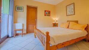 Een slaapkamer met een houten bed, een stoel, een nachtkastje met een lamp en een deur.
