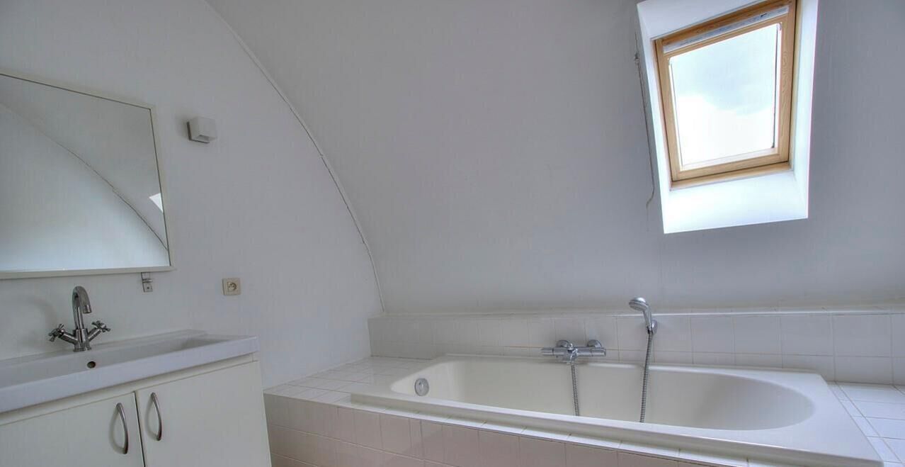 Ein modernes Badezimmer mit einer frei stehenden Badewanne, einem großen Spiegel und einem Oberlicht.