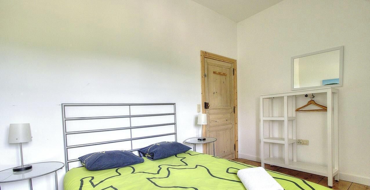 A bedroom with a bed, bedside table, lamp, wardrobe, and a door.