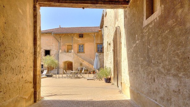 Une cour ouverte avec un bâtiment au style rustique, des sièges en plein air et une plante en pot.
