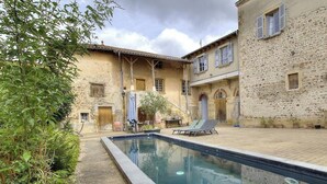 Une cour avec une piscine, des bâtiments en pierre et des espaces de détente en plein air.