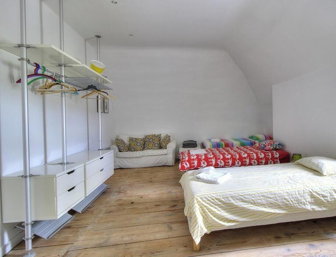Un dormitorio con cama elevada, un armario blanco, una percha para ropa y un pequeño sofá.