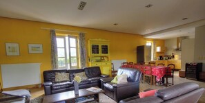 A living room with a fireplace, a dining area with a red tablecloth, and a kitchen area with cabinets and a refrigerator.