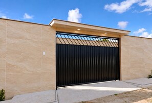 A modern building with a large black gate, beige walls, and a clear sky.