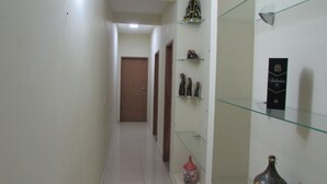 A narrow hallway with a wooden door at the end, glass shelves with decorative items, and a bottle on the right. - Casa Aconchegante em Santa Cruz Cabrália -Ba (Santa Cruz Cabrália)