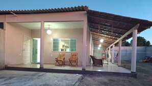 A covered outdoor area with a patio, two wooden chairs, a table, and a brick fireplace. - Casa Aconchegante em Santa Cruz Cabrália -Ba (Santa Cruz Cabrália)