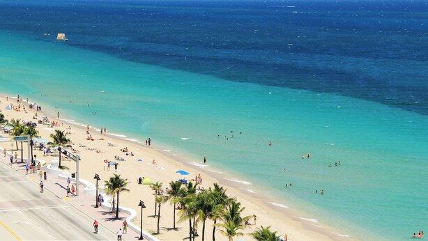 Una playa con aguas turquesas cristalinas, palmeras y un amplio paseo marítimo.