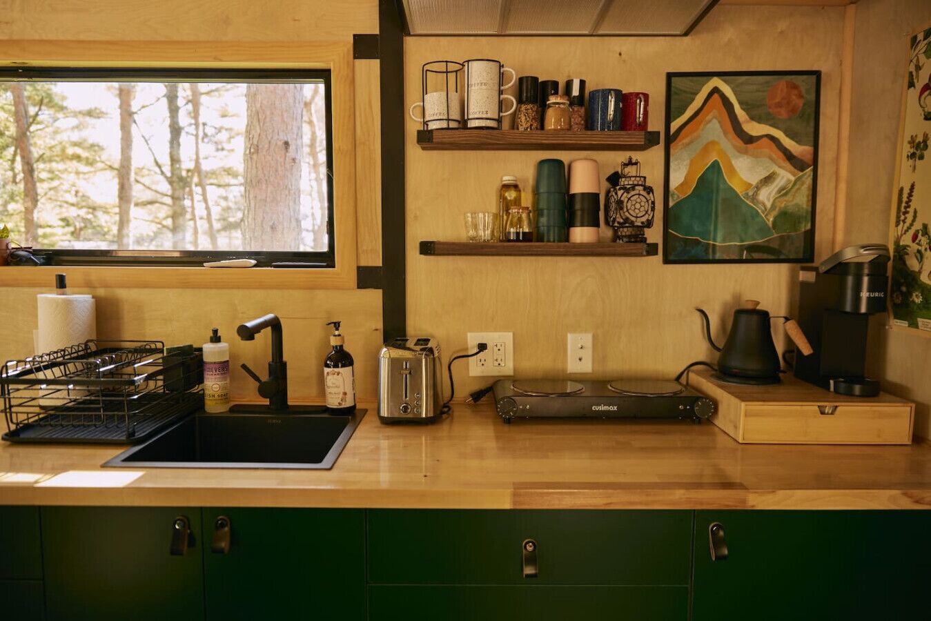 A kitchen with a wooden countertop, a sink, a toaster, a coffee maker, and a shelf with various items.