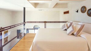 A modern hotel room with a large bed, a glass balcony, and a view of the city.