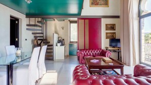 A modern living room with a glass coffee table, red leather sofas, and a staircase leading to a kitchen.
