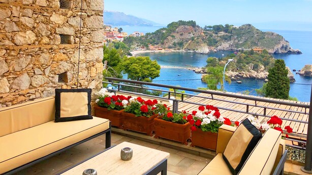 A balcony with stone walls, outdoor seating, and flower planters.
