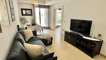 En moderne stue med en sofa, et fladskærms-TV og et spiseområde med et bord og stole.