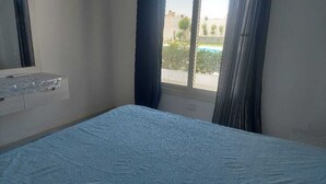 Um quarto com cama, janela com cortinas e uma pequena prateleira com espelho.