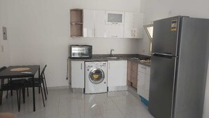 Uma cozinha compacta com máquina de lavar, frigorífico, micro-ondas e um espaço de refeições com mesa e cadeiras.