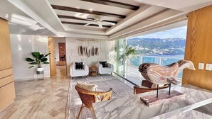 A modern living room with a large window, a marble coffee table, and a view of a coastal landscape.
