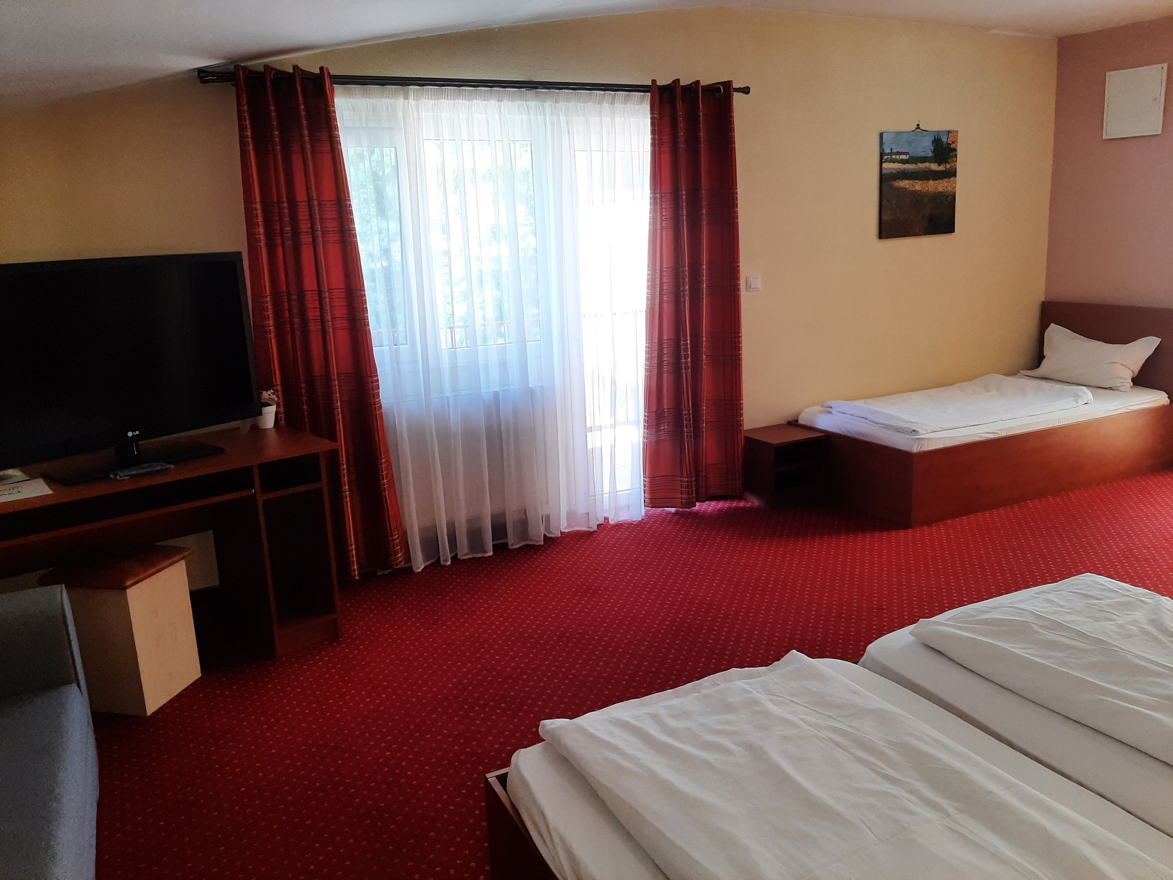 Een hotelkamer met een bed, televisie, bureau en raam met gordijnen.