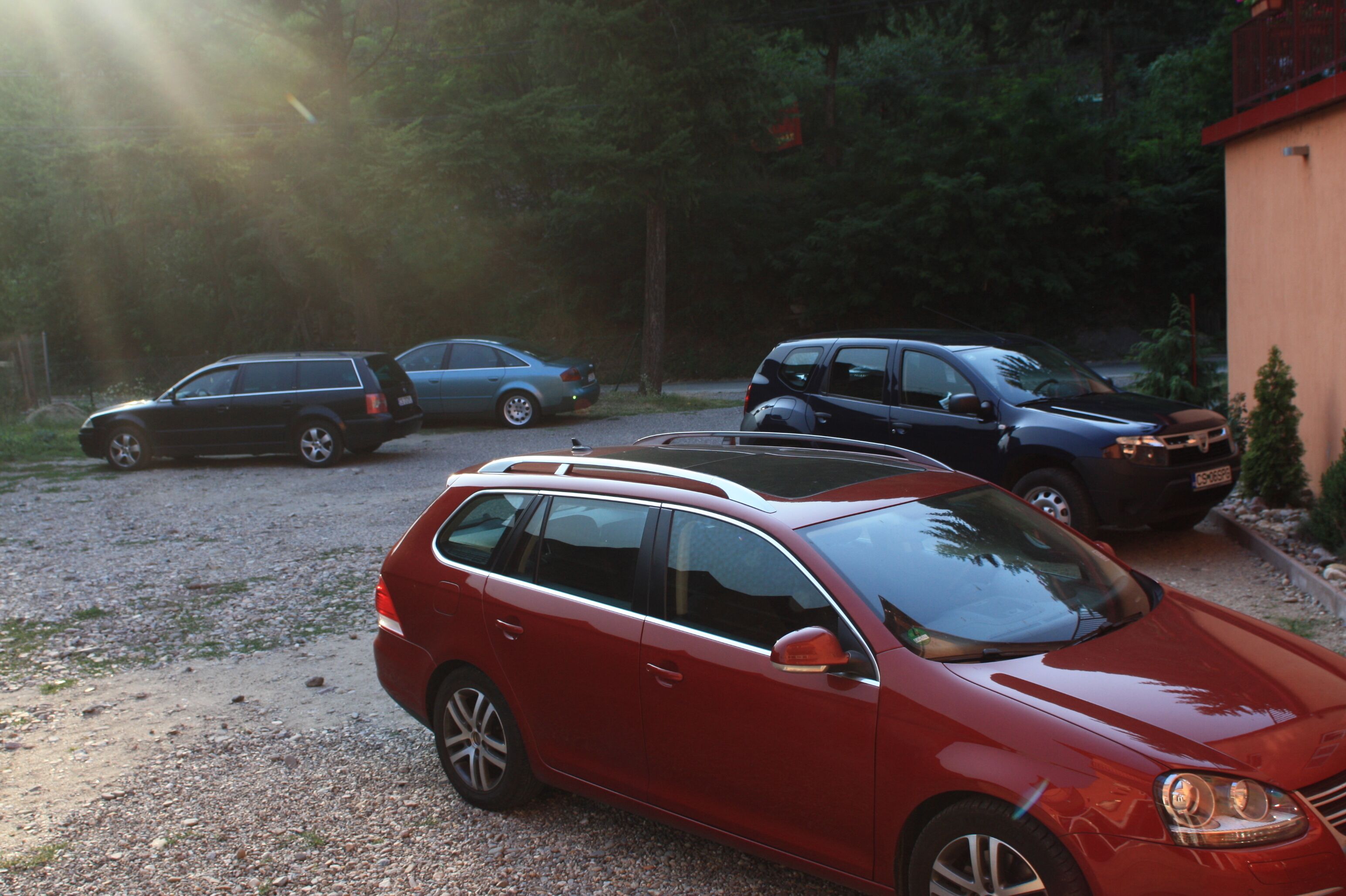 A red station wagon parked in a gravel driveway with other vehicles.