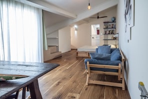 Un espace de vie de style loft avec une table à manger en bois, un canapé bleu et un escalier menant à un niveau supérieur.