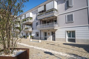 Un immeuble à plusieurs étages doté de balcons, d’une cour pavée et d’un arbre.