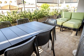 Una terraza con una mesa y sillas, un sofá y vistas a edificios y árboles.