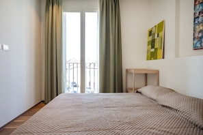 Une chambre à coucher avec un lit, une fenêtre avec des rideaux, une petite table et un tableau accroché au mur.