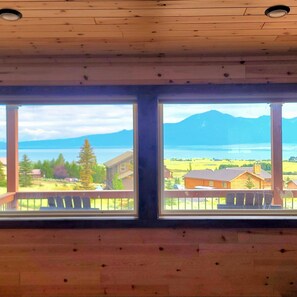 Une pièce dotée de deux grandes fenêtres donnant sur un lac, des montagnes et un quartier résidentiel.